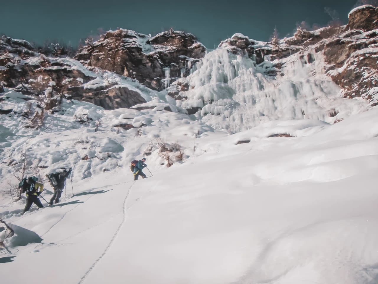 Groupe d'aventuriers escaladant une montagne enneigée, avec des cascades de glace en arrière-plan.