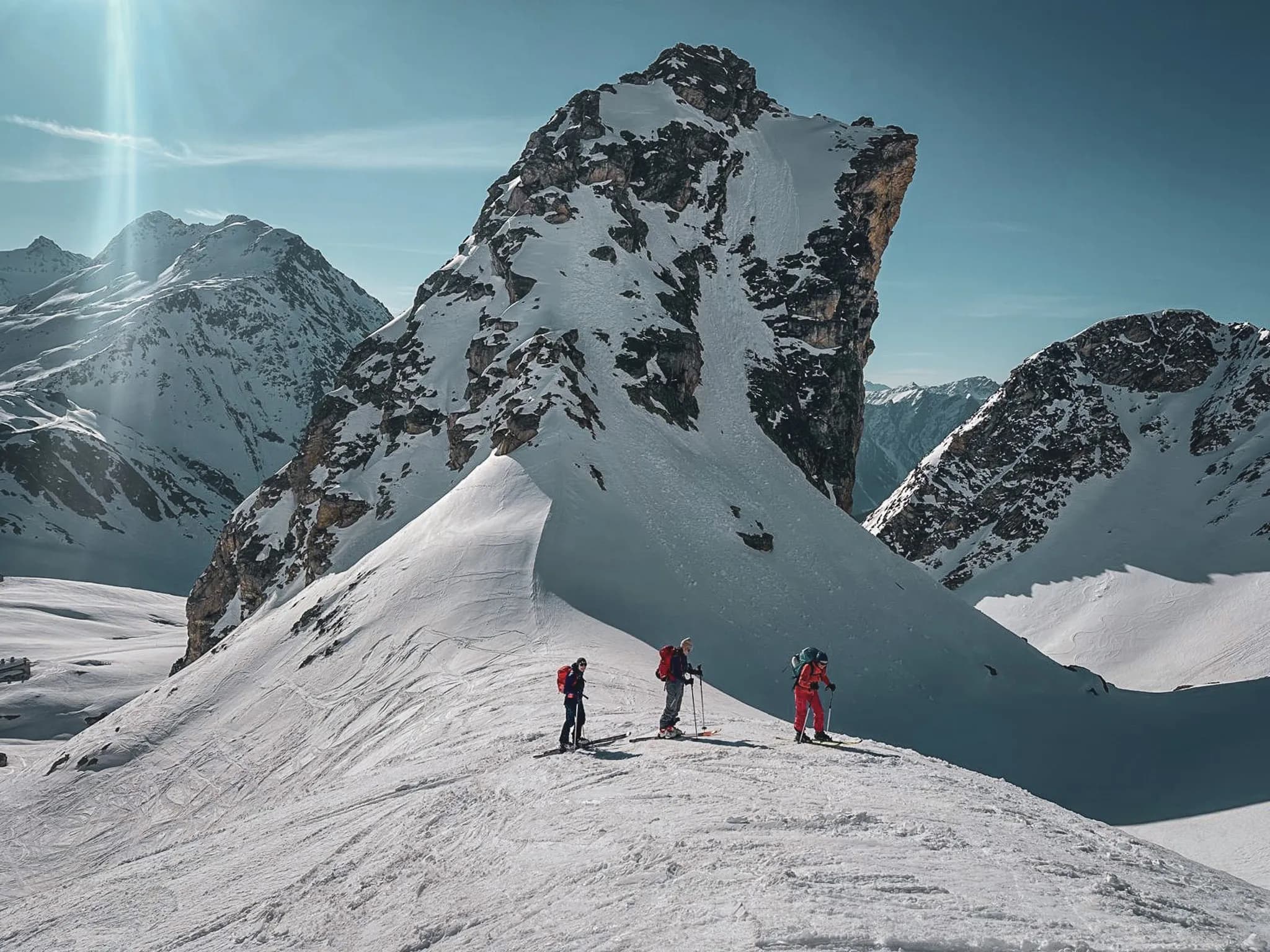 Three skiers explore a majestic alpine landscape, surrounded by snow-capped peaks.