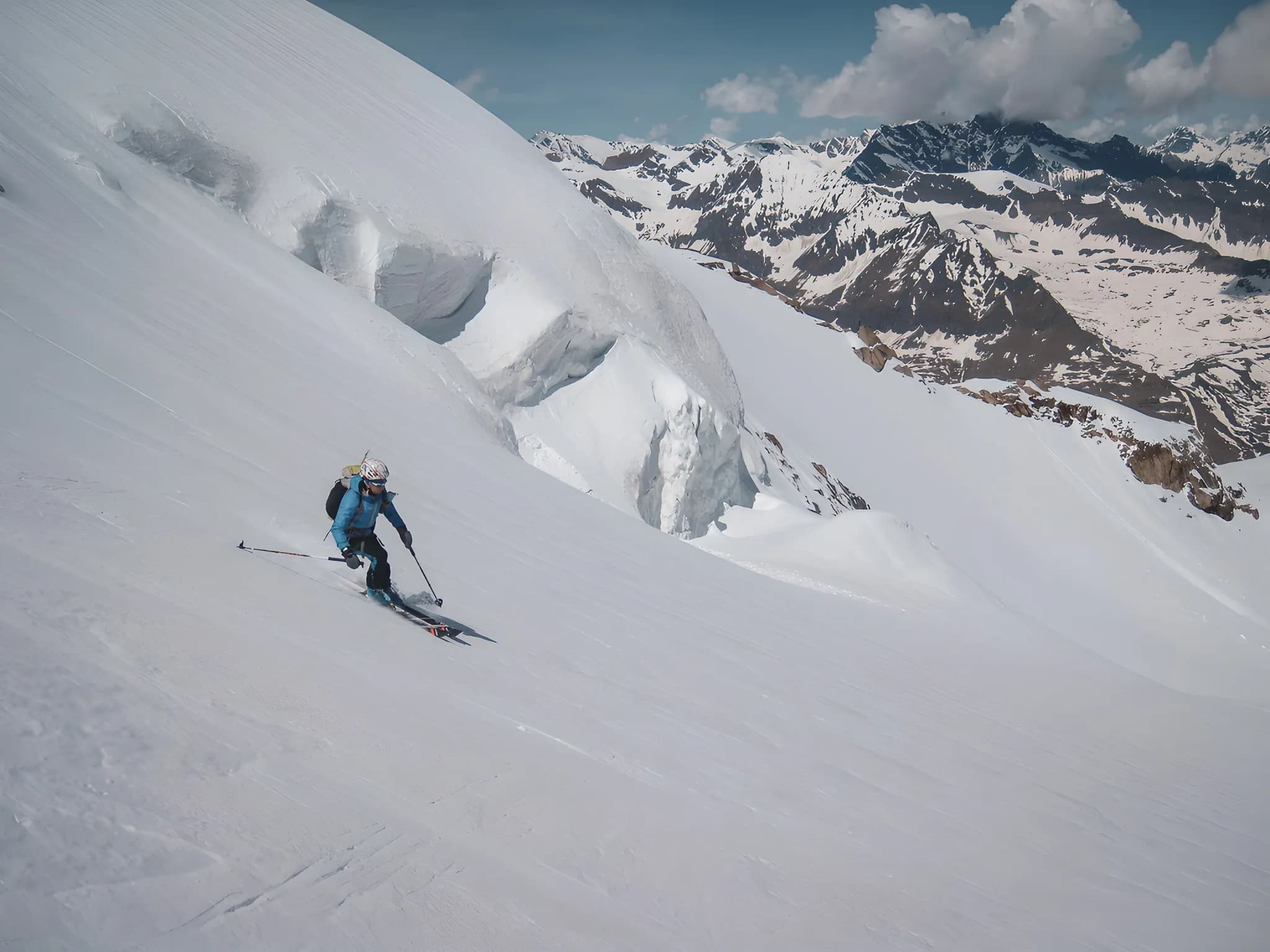 Un skieur descend une pente enneigée, entouré de montagnes majestueuses sous un ciel clair.