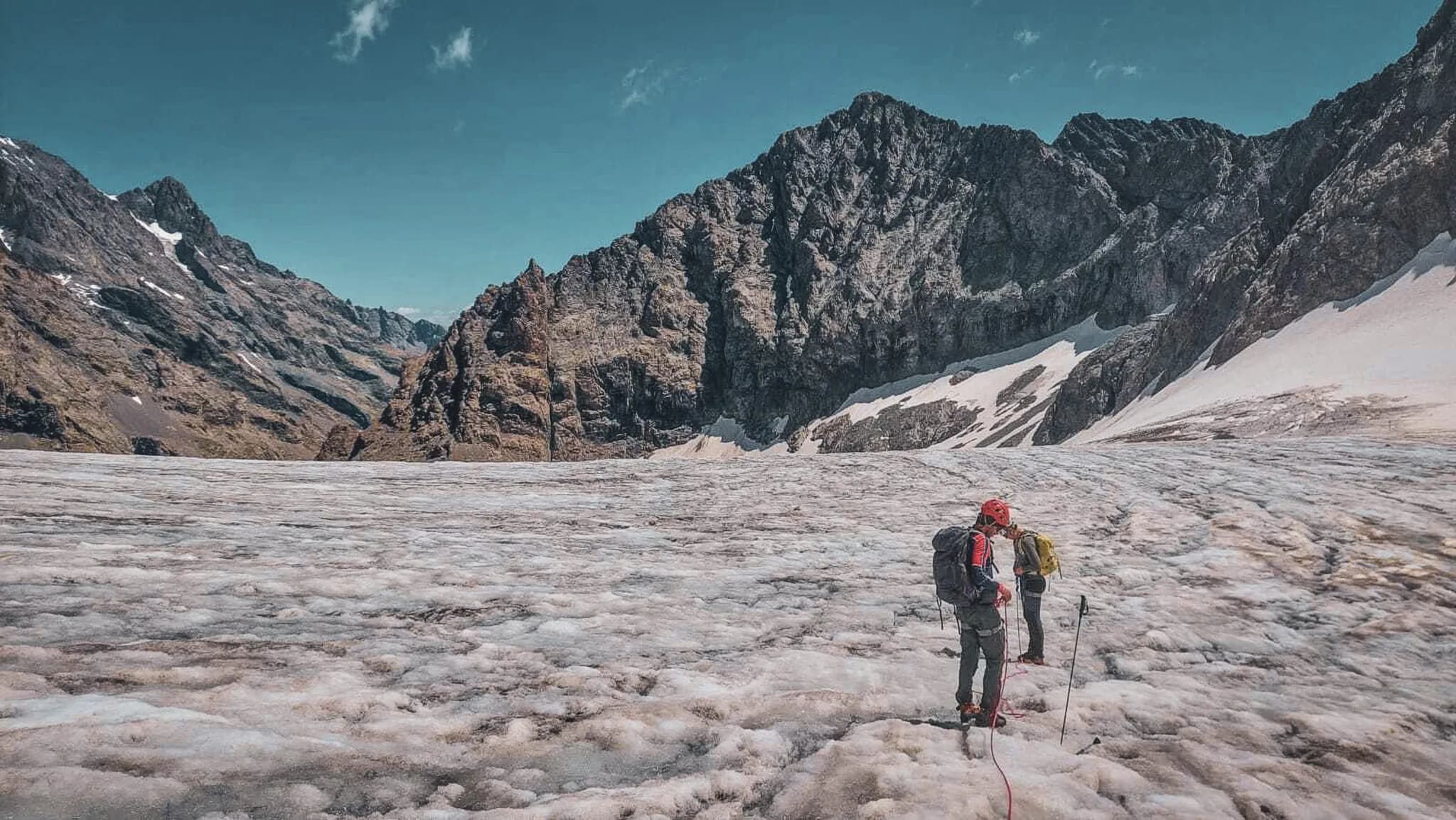 Twee klimmers op een gletsjer, omringd door het majestueuze Ecrins-gebergte onder een blauwe hemel.