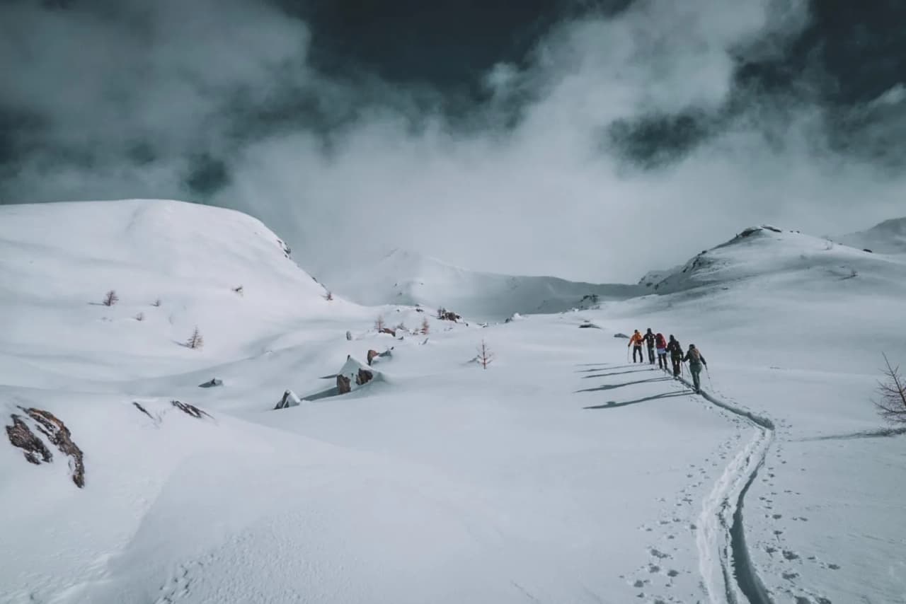 Groupe de randonneurs sur un sentier enneigé, entouré par les majestueuses Alpes italiennes.