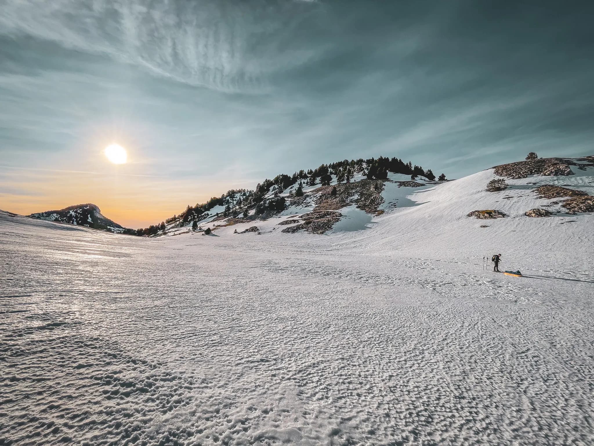 "Besneeuwd landschap van de Vercors bij zonsondergang, avonturier met pulka op wild terrein."