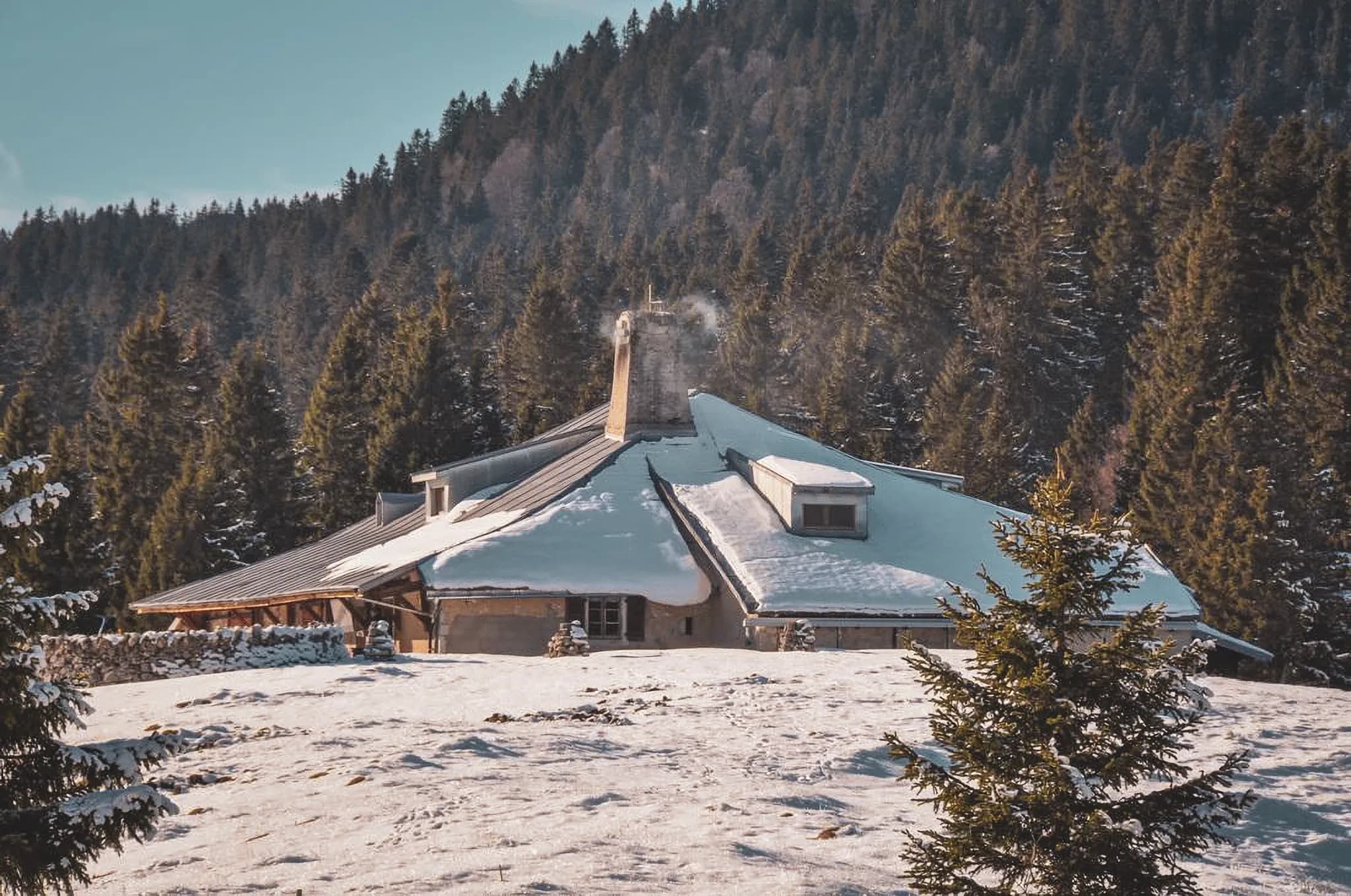 Een besneeuwd chalet in de Zwitserse Jura, omringd door majestueuze dennenbomen en een vredig landschap.