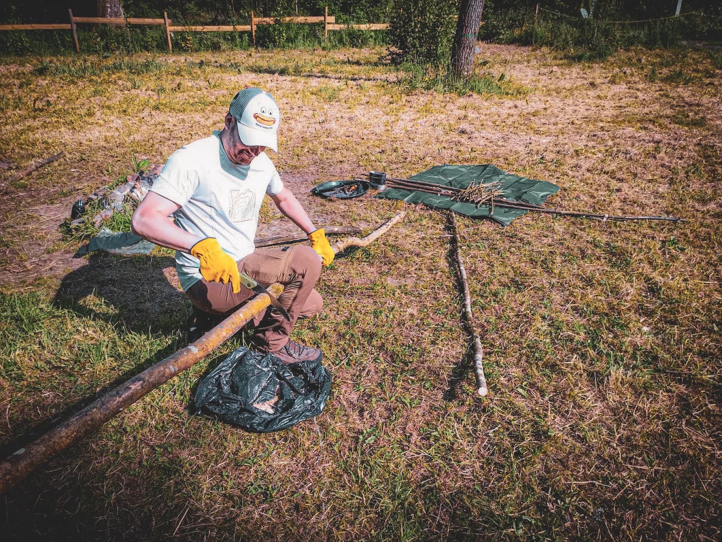 Een deelnemer aan een survivalcursus snijdt een stok in het zonnige groen van de Belgische Ardennen.