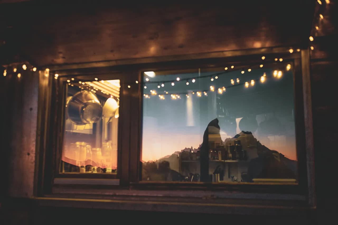 Reflet d'un paysage montagneux au crépuscule dans une fenêtre illuminée, ambiance chaleureuse.