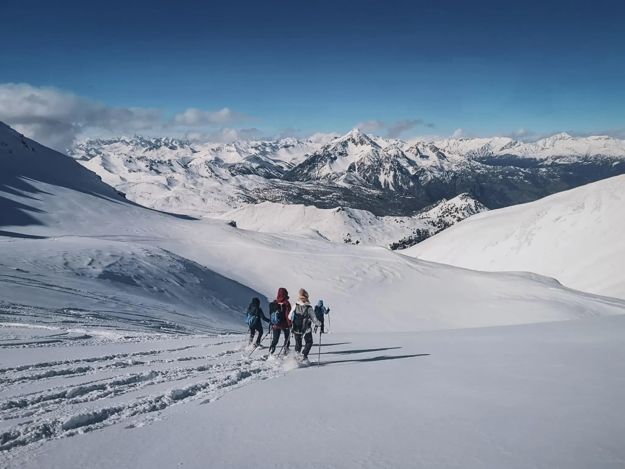 Snowshoe hikers traversing snow-covered landscapes with majestic mountains in the background.