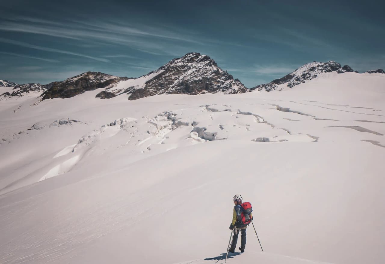 Un alpiniste contemplant un vaste glacier sous un ciel bleu, face aux majestueux sommets alpins.