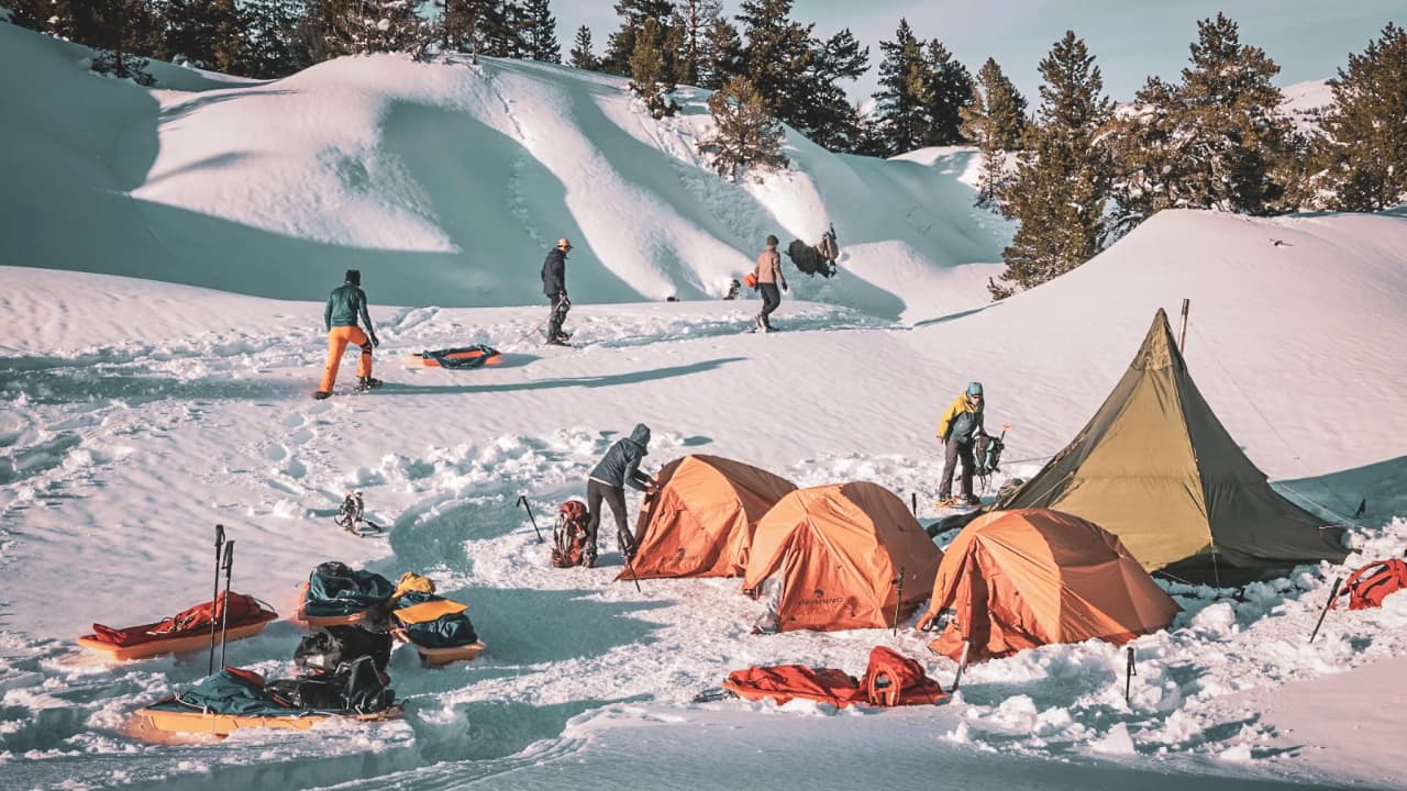 Groupe d'aventuriers en pleine préparation de bivouac sous un ciel dégagé, au cœur de la neige.