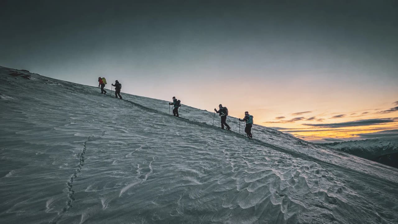 Een groep avonturiers die bij schemering een besneeuwde helling beklimmen, in een magische en ruige sfeer.