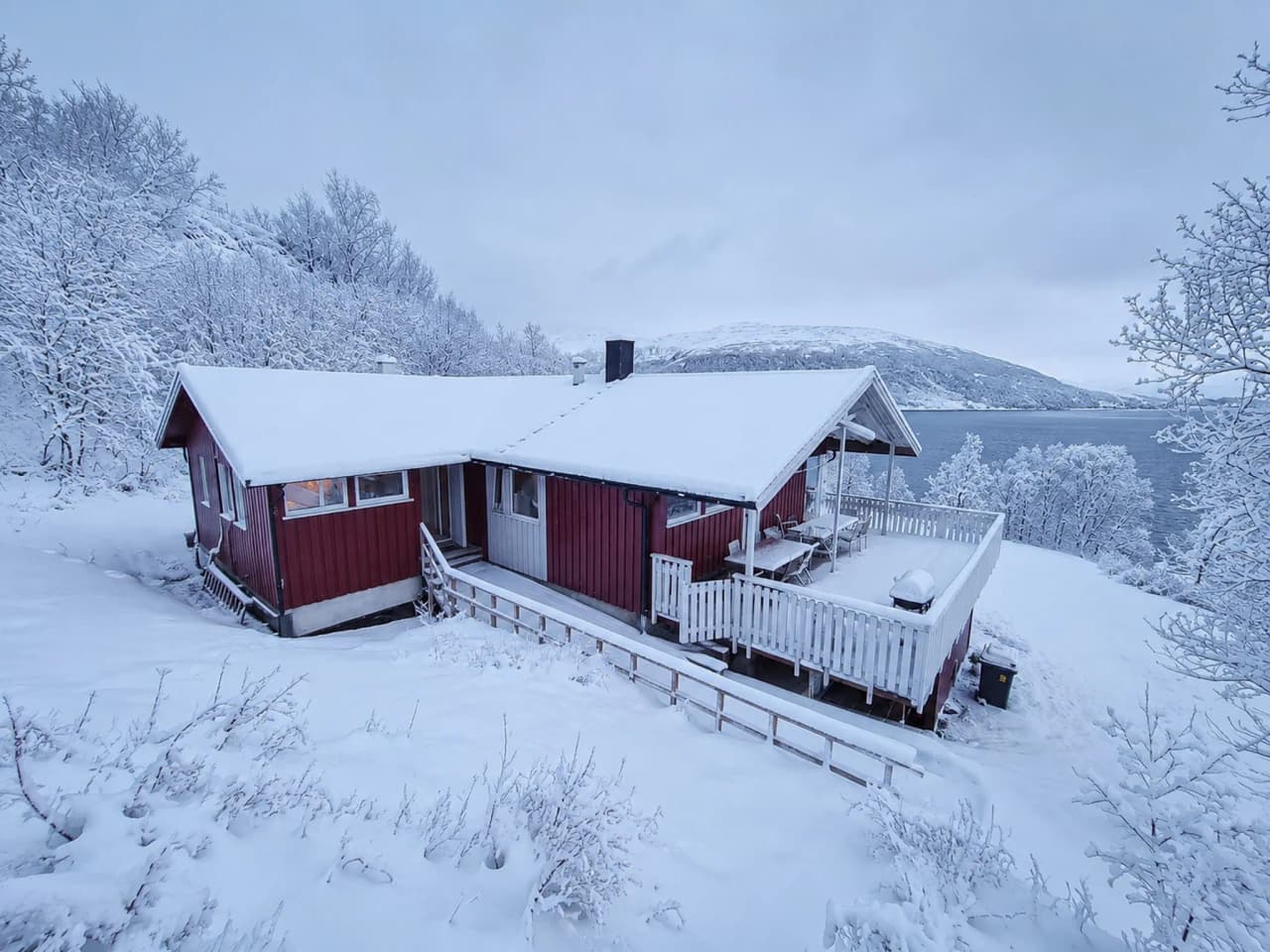 Een rood houten chalet onder de sneeuw, omgeven door vredige arctische landschappen in Tromsø.