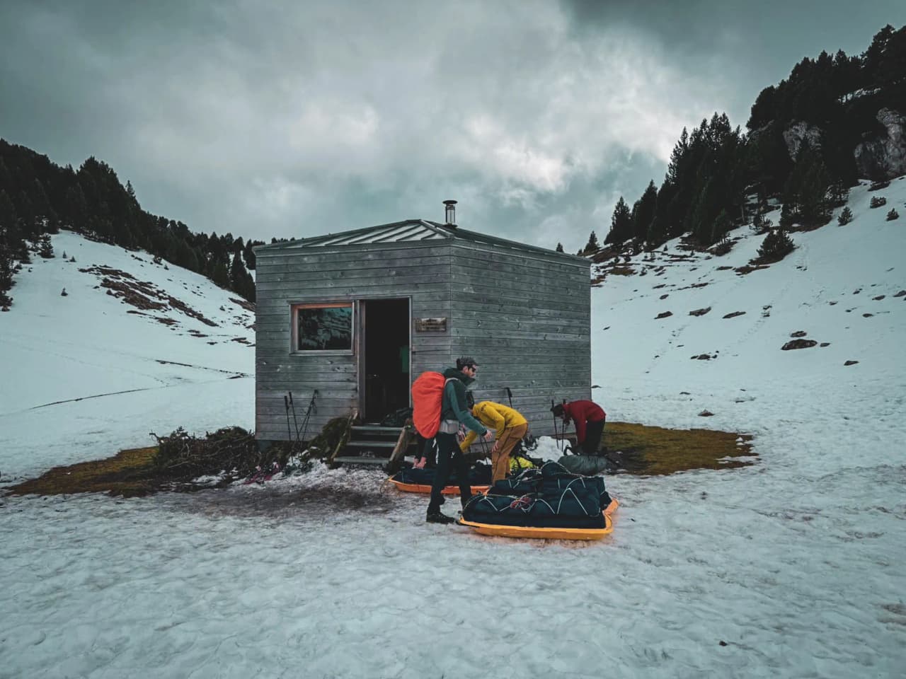 Group of adventurers preparing their equipment near a wooden chalet, majestic snowy landscape.