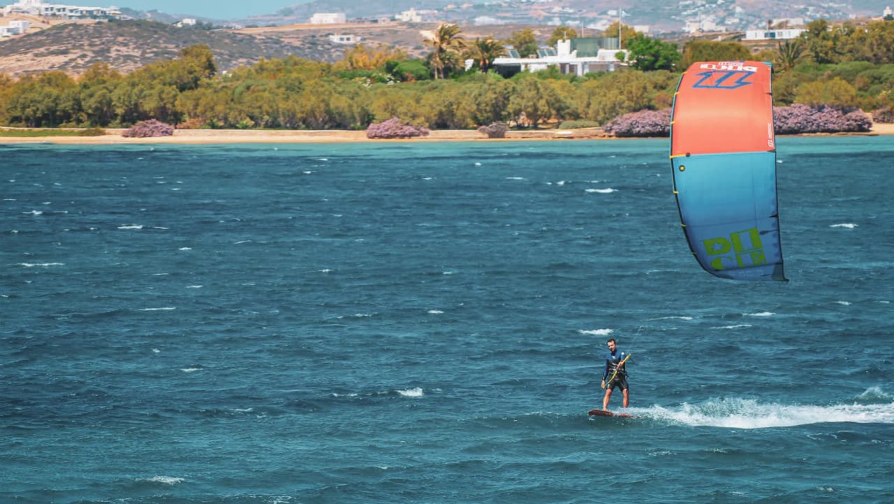 Kitesurfeur glissant sur des eaux turquoise, entouré de paysages ensoleillés des Cyclades.