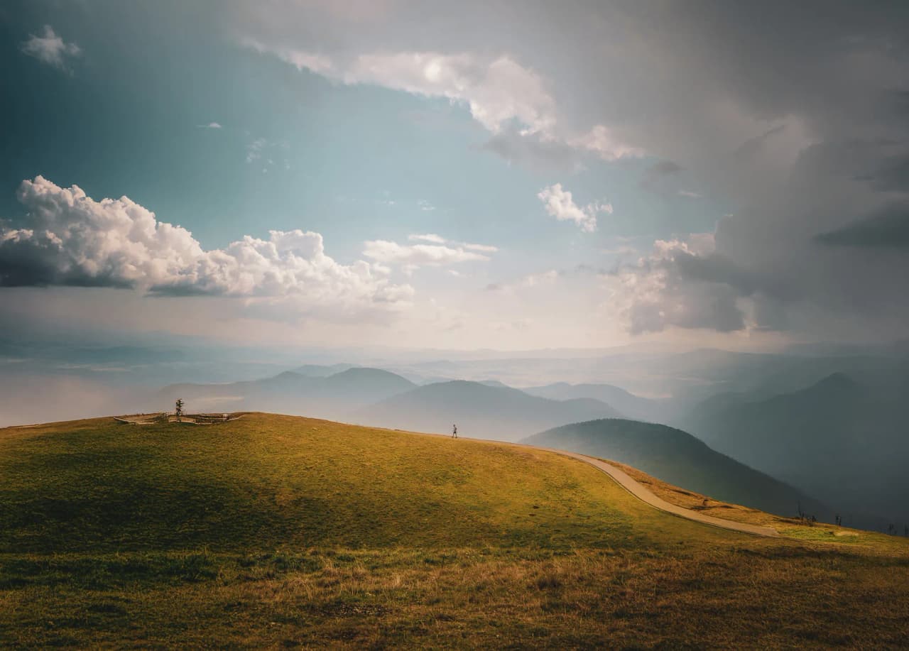 A runner on a green path facing the mountains under a dramatic Auvergne sky.