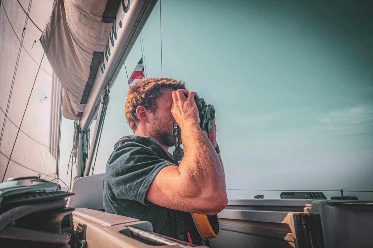 Een man bekijkt de horizon door een verrekijker terwijl hij langs de wilde kust van Bretagne vaart.