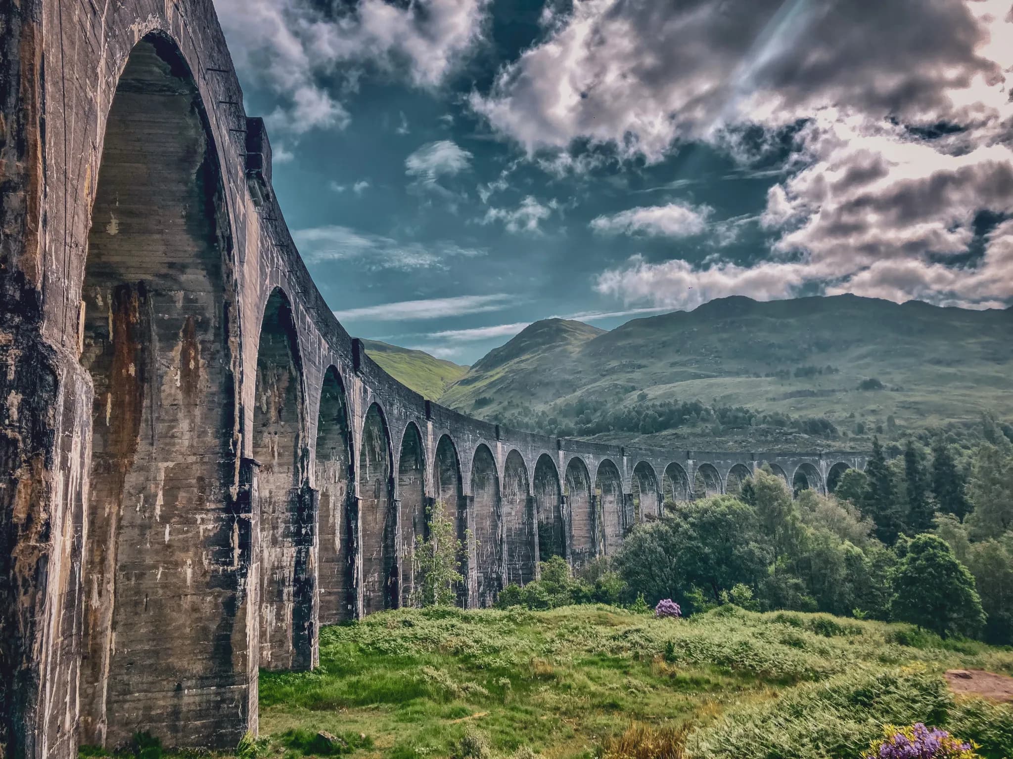 Een majestueus viaduct dat uittorent boven de groene valleien van de Highlands, onder een dramatische hemel.
