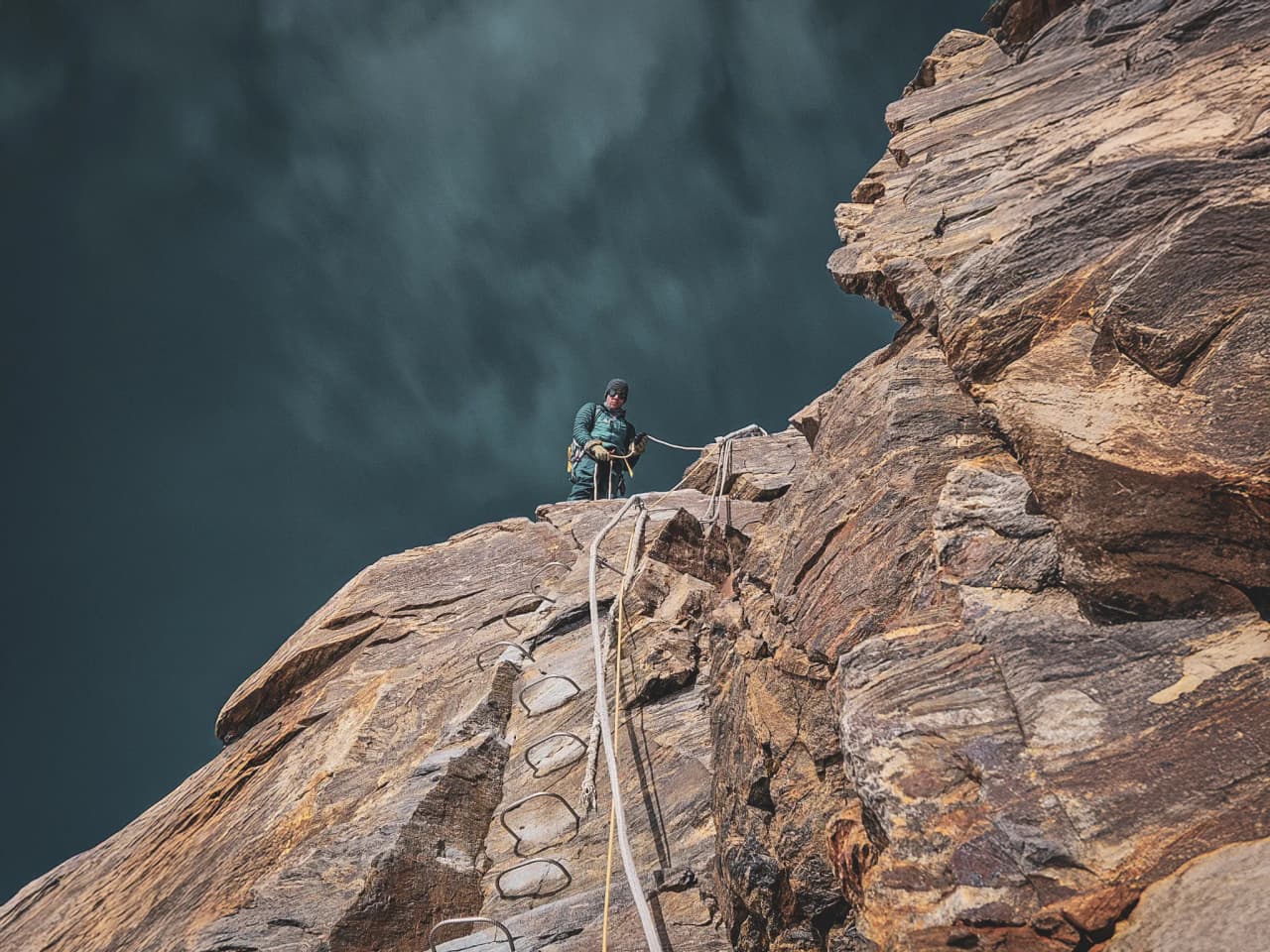 Mountaineer climbing a rock face, dramatic sky in the background.