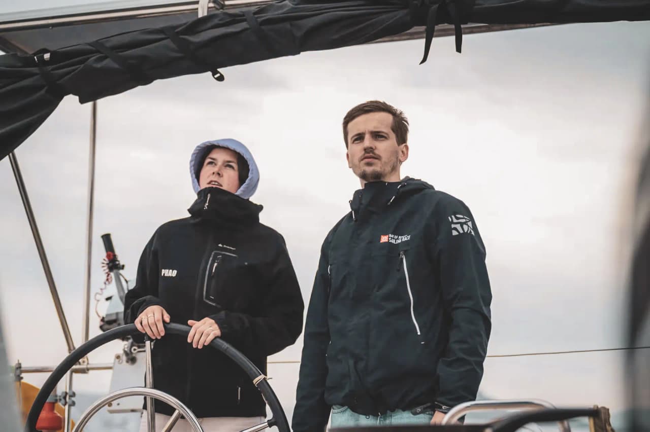 Deux navigateurs concentrés sur un voilier, prêts à explorer les îles grecques sous un ciel nuageux.