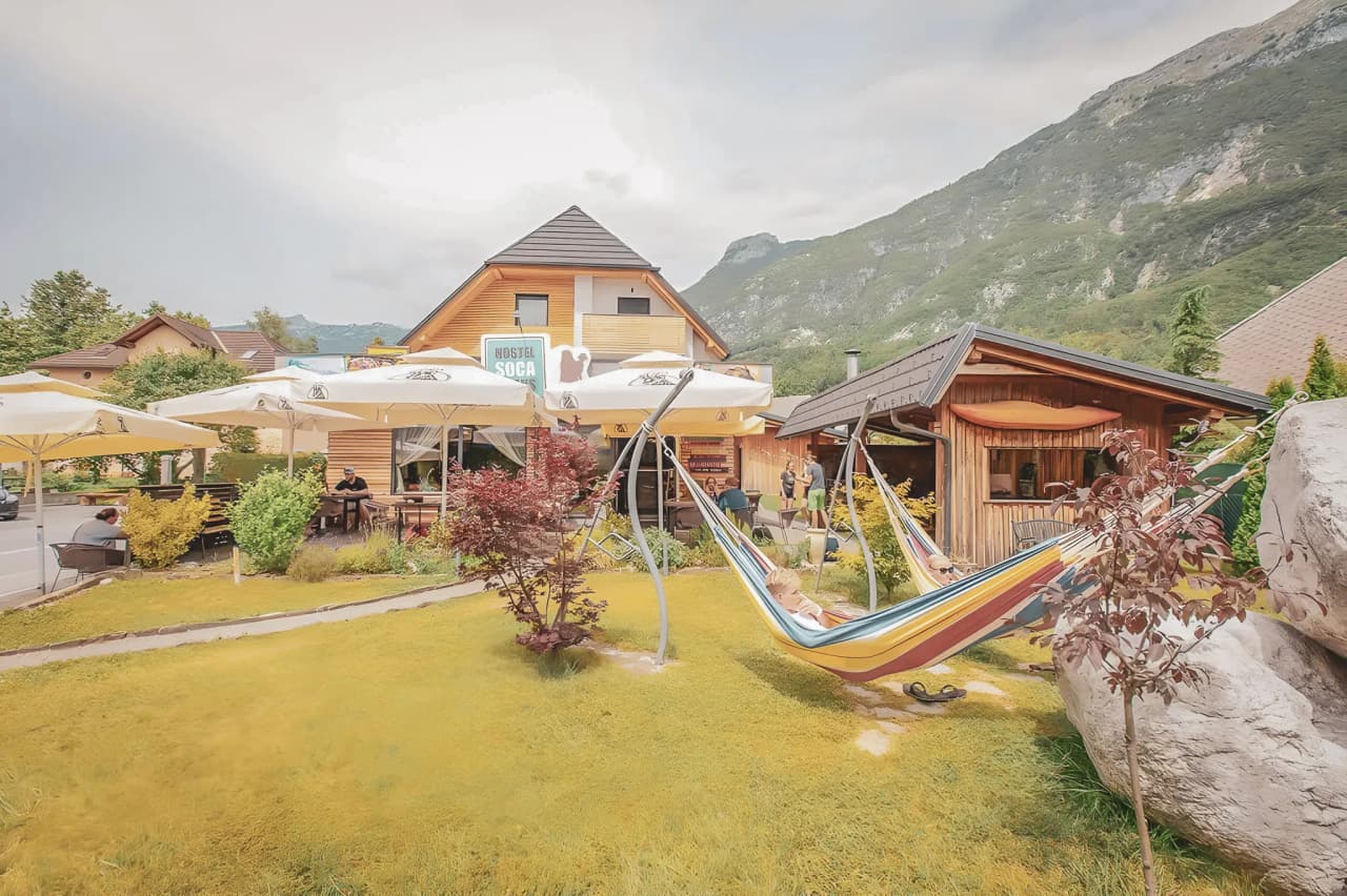 A charming Mountain hut surrounded by greenery, with colourful hammocks and mountains in the background.