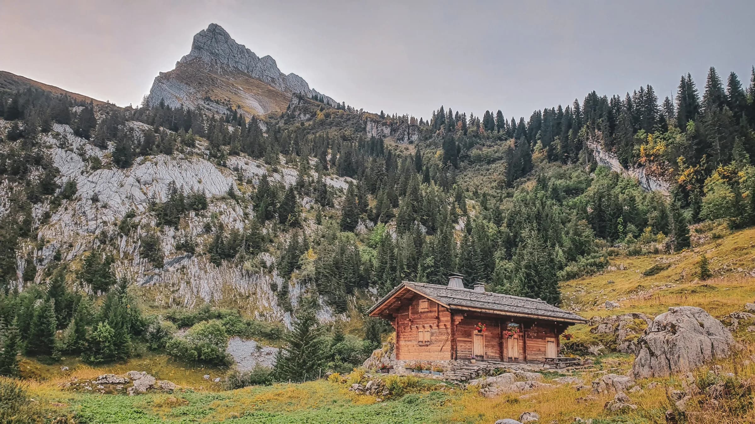 A wooden cabin in the heart of the Alps, surrounded by majestic peaks and greenery.