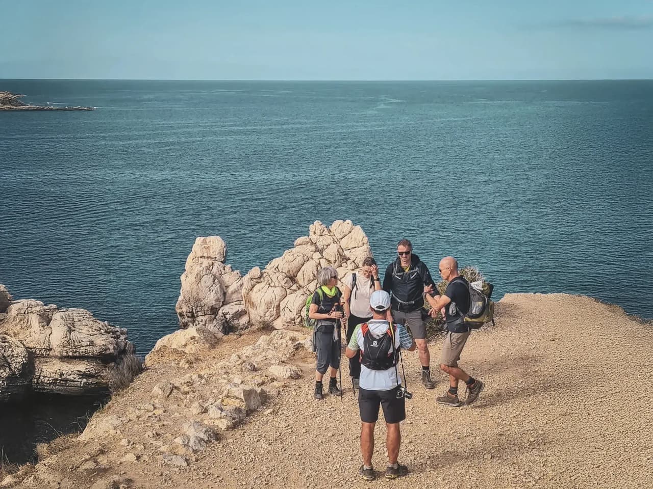 Groupe de randonneurs réunis sur un promontoire, face à la mer turquoise de Majorque.