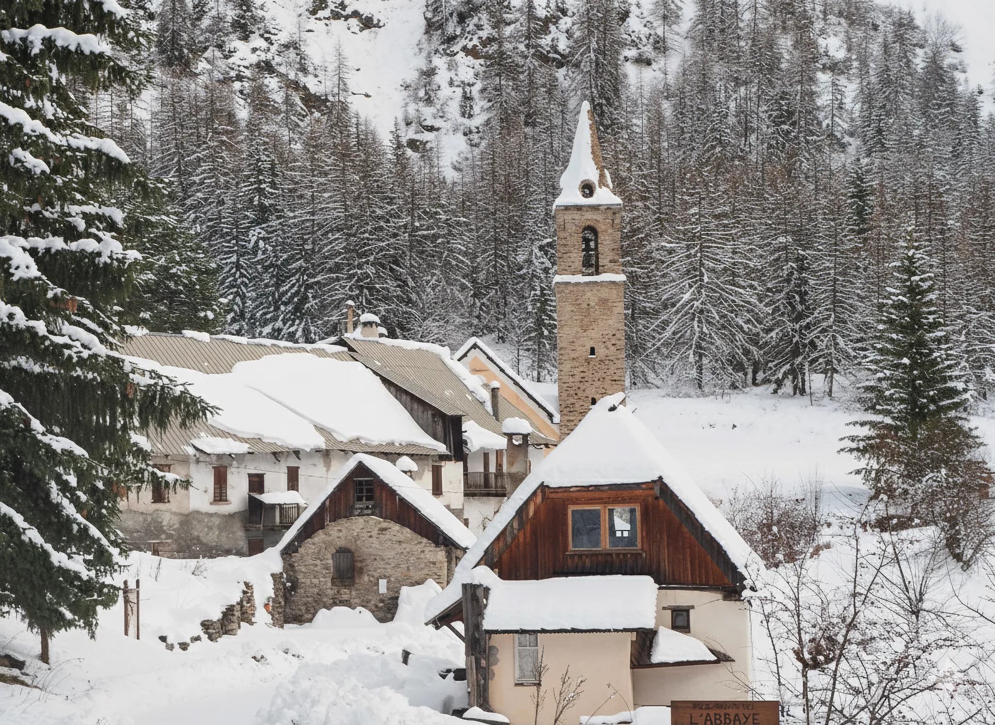 Charmant village enneigé au bord d'une forêt, avec un clocher pittoresque sous une douce lumière hivernale.
