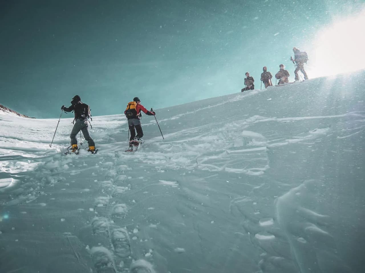 Groupe de randonneurs s'élevant sur une pente enneigée sous un ciel bleu lumineux.