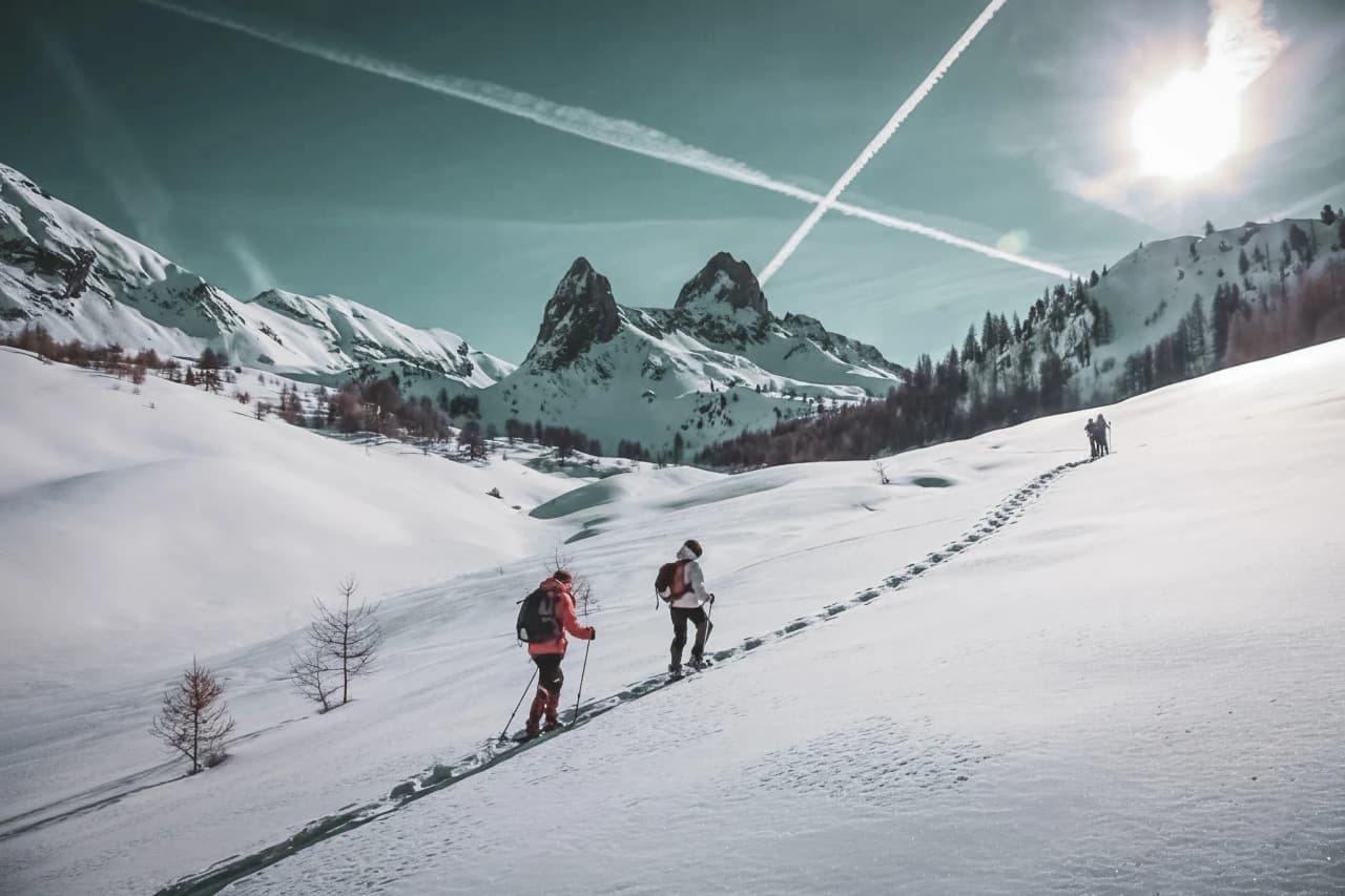 Randonneurs à raquettes sur un paysage enneigé avec montagnes majestueuses en arrière-plan.