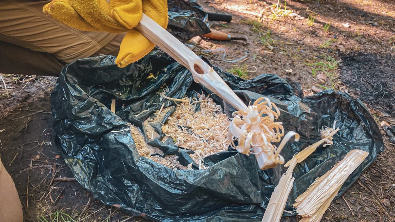 Un participant à un stage de survie en forêt montre des copeaux de bois pour allumer un feu.