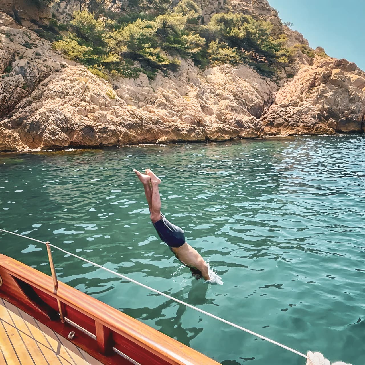 Un plongeur s'élance dans les eaux cristallines des Calanques, entouré de falaises dorées.