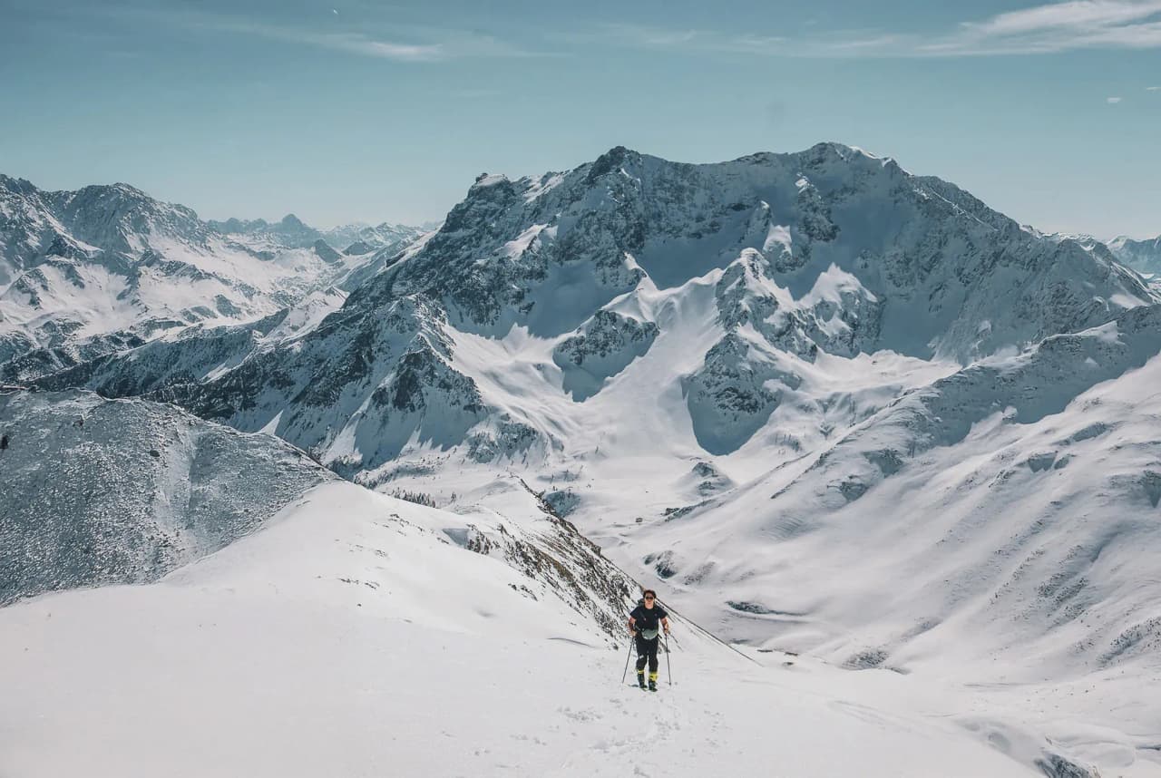 A lone skier climbing majestic snow-capped peaks under a brilliant blue sky.