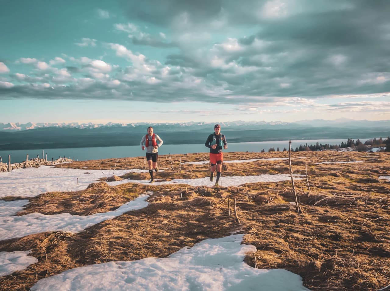 Twee hardlopers vertrekken over een alpenpad, omringd door sneeuw en een spectaculair berglandschap.