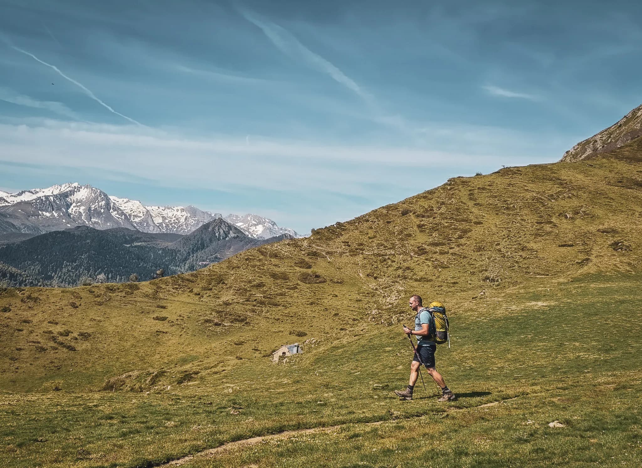 Randonnée dans les Pyrénées, un aventurier explore de verdoyantes collines sous un ciel ensoleillé.