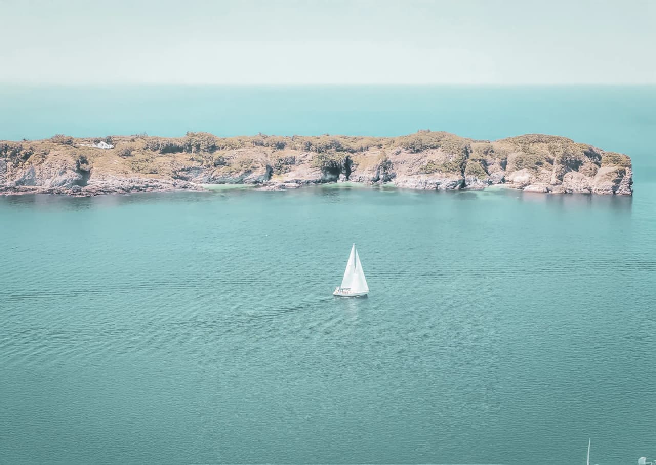 Voguez à la voile sur des eaux turquoises, avec une île en toile de fond. Une invitation à l’évasion.