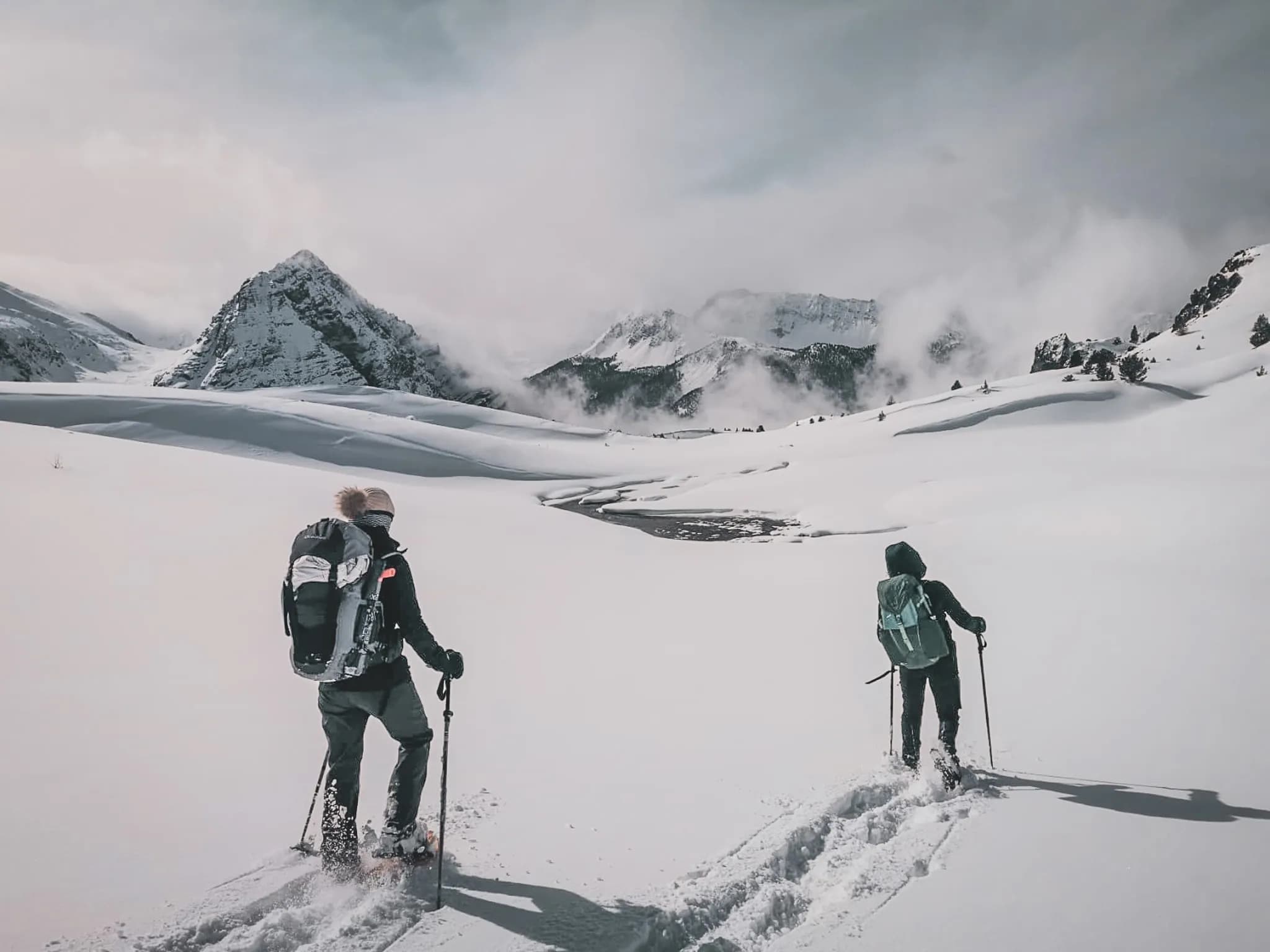 A group of hikers venture into a grandiose snowy landscape, with majestic mountains in the background. The ground is covered with a thick layer of fresh snow, and snakes' footprints can be seen.
