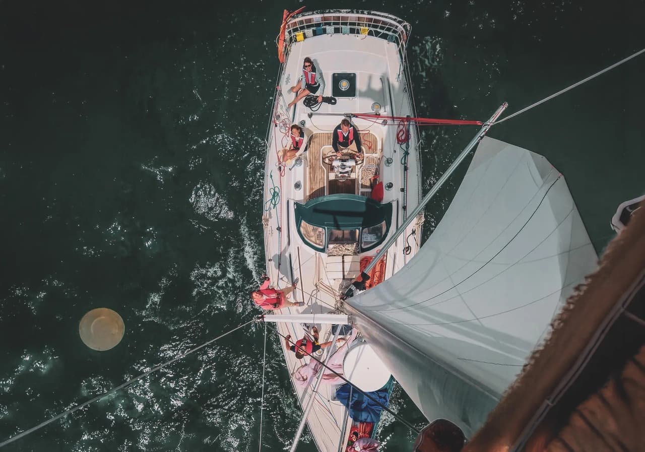 A sailboat on the open sea, an active crew manoeuvring under clear skies, a promise of adventure.