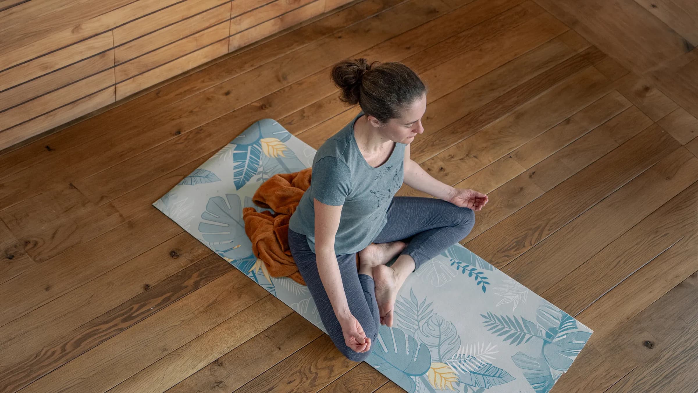 Femme méditant paisiblement sur un tapis de yoga, dans un cadre enchanteur en bois naturel.