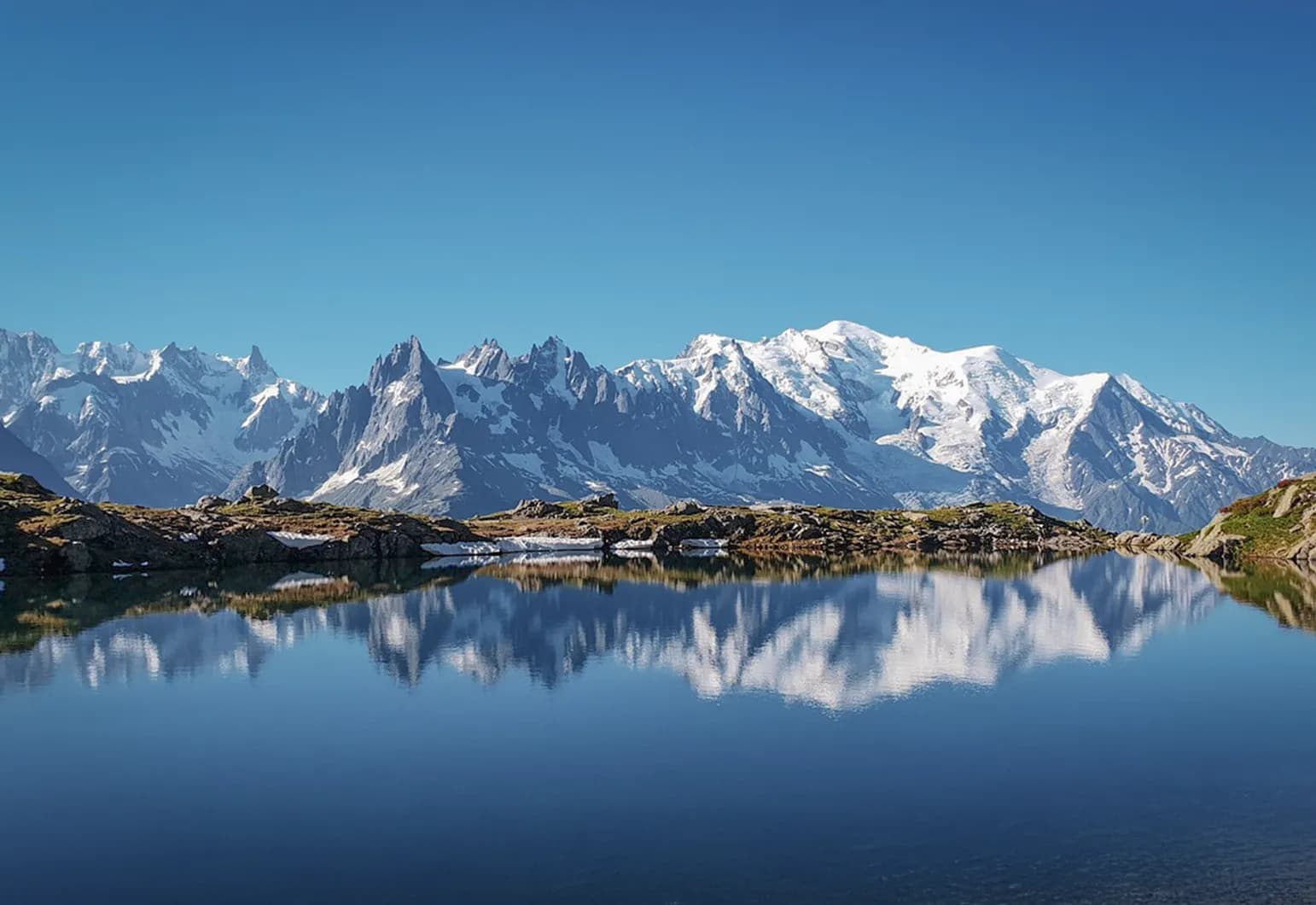 Majestic snow-capped mountains reflected in a crystal-clear lake under a blue sky.