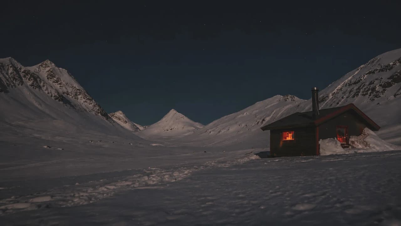 Een gezellige hut onder een sterrenhemel, omringd door besneeuwde bergen in Noors Lapland.