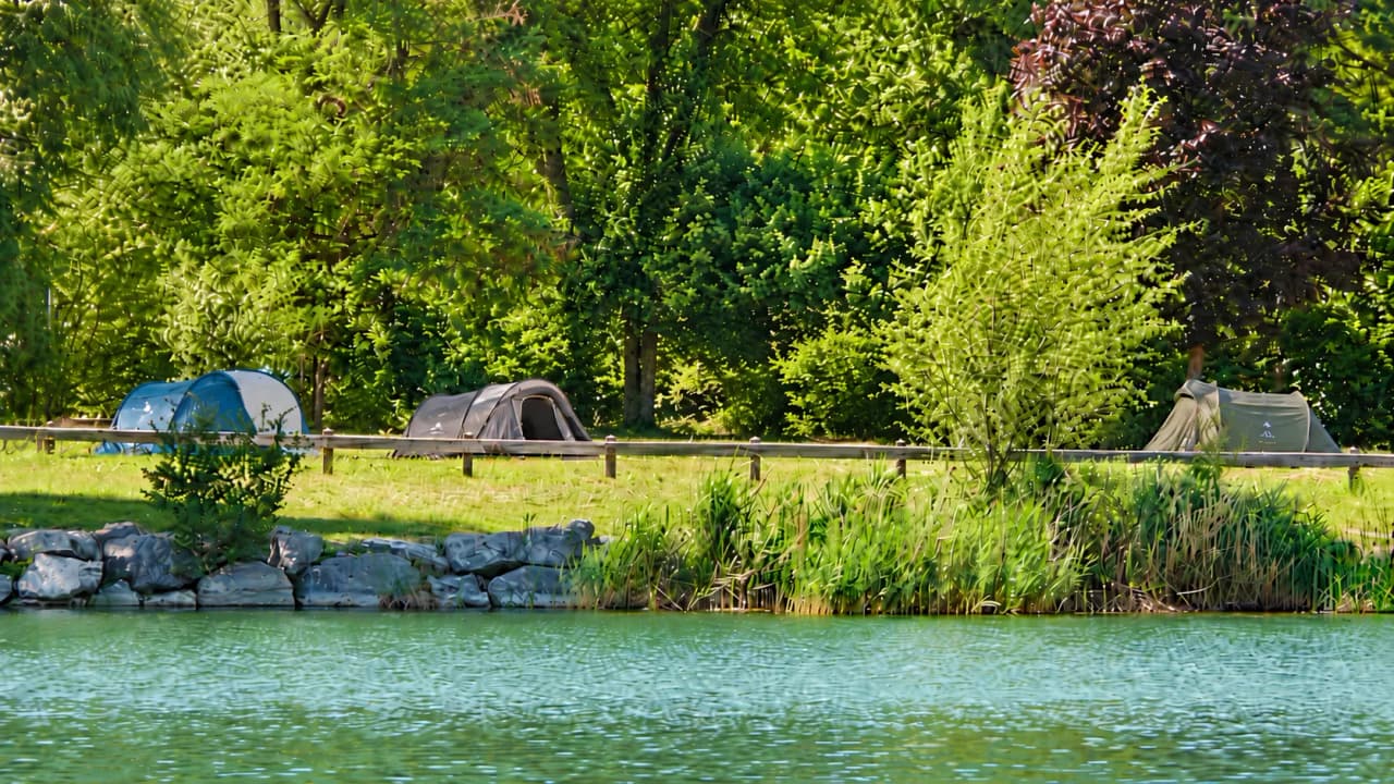 Kleurrijke tenten aan de oever van een rivier, omgeven door weelderig groen, een vredige sfeer en de natuur.