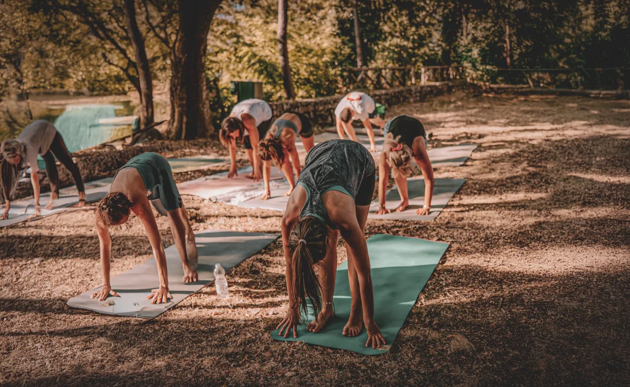 Een groep mensen beoefent yoga in de buitenlucht, onder zonnige bomen.