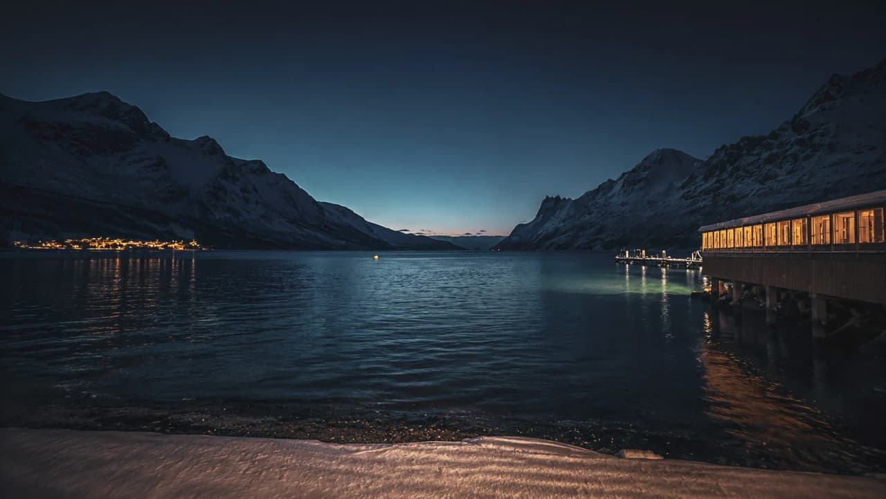 Een vredig uitzicht op een fjord met besneeuwde bergen bij zonsondergang, dat uitnodigt tot avontuur.