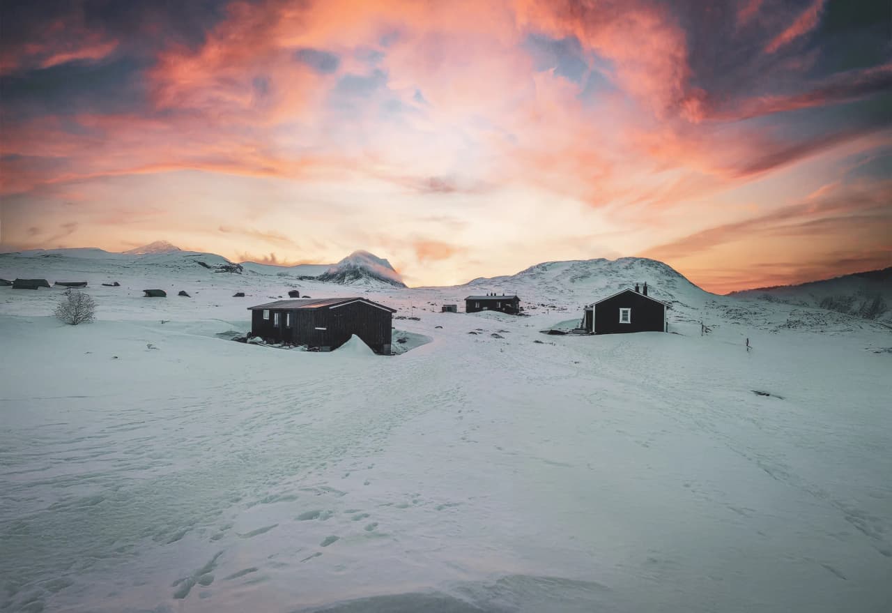 Snow-covered cabins under a colourful sky, a magical landscape in Swedish Lapland that invites adventure.