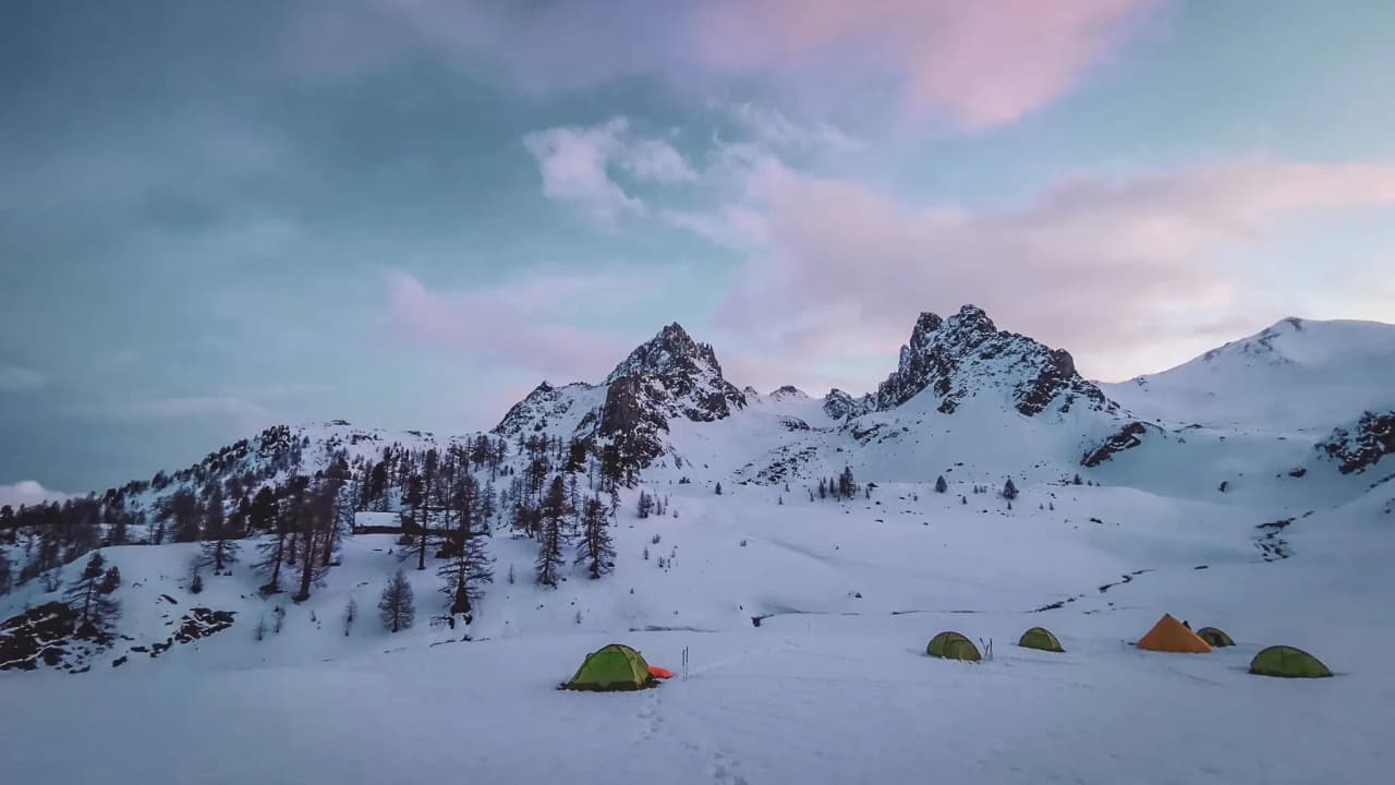 Camping hivernal dans le massif des Cerces, entouré de montagnes enneigées et d'un ciel pastel.