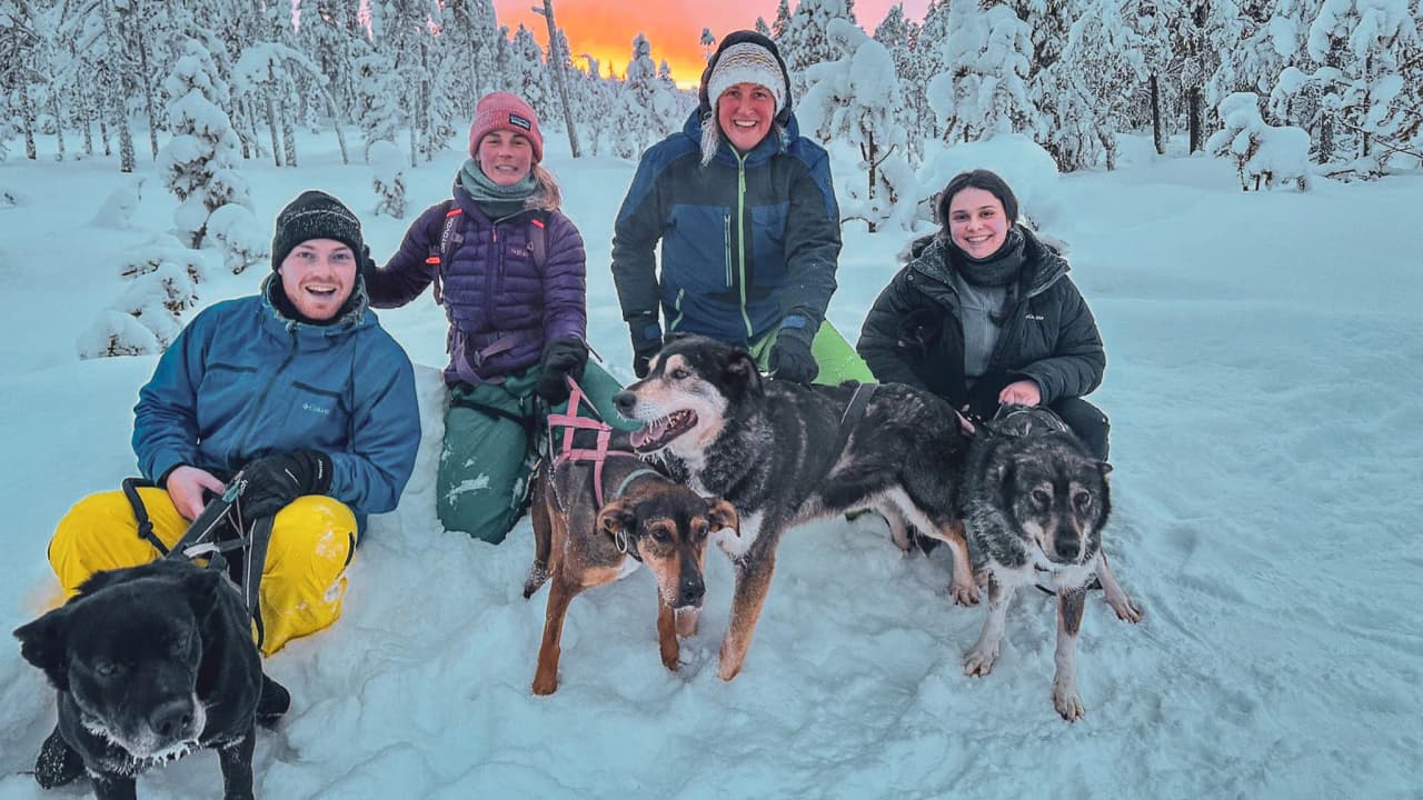 A happy group with sled dogs in a snowy Lapland landscape at sunset.
