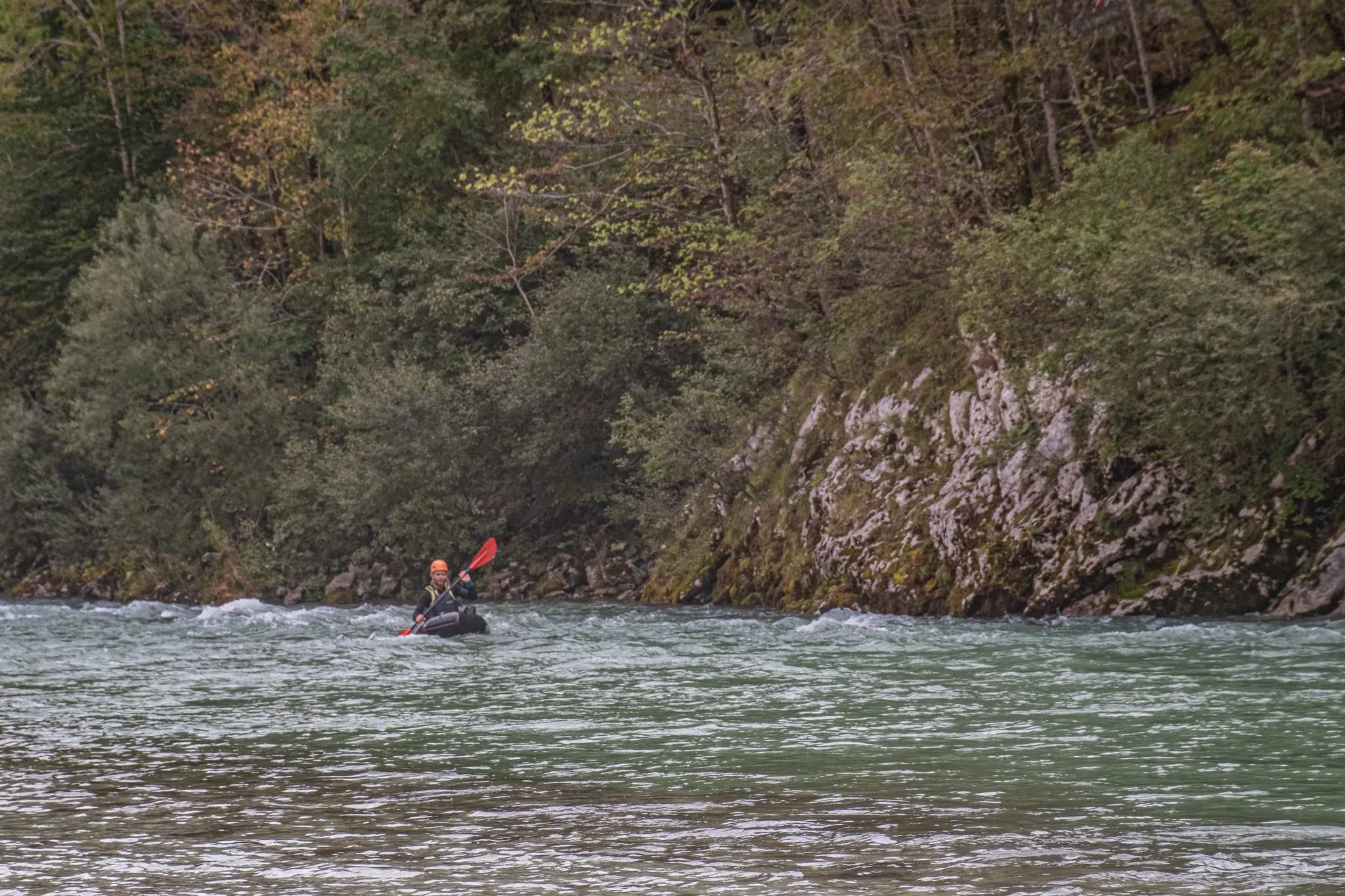 Une aventurière pagaye en packraft sur une rivière turquoise entourée de forêts verdoyantes.