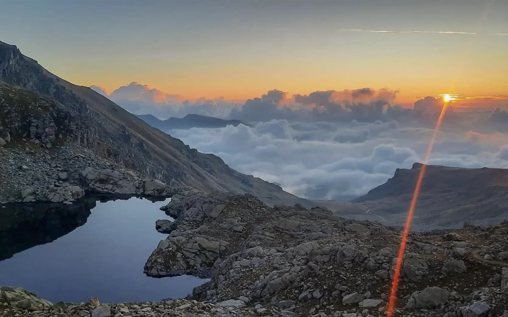 Dazzling sunrise over a mountain lake surrounded by clouds, a wild and soothing landscape.