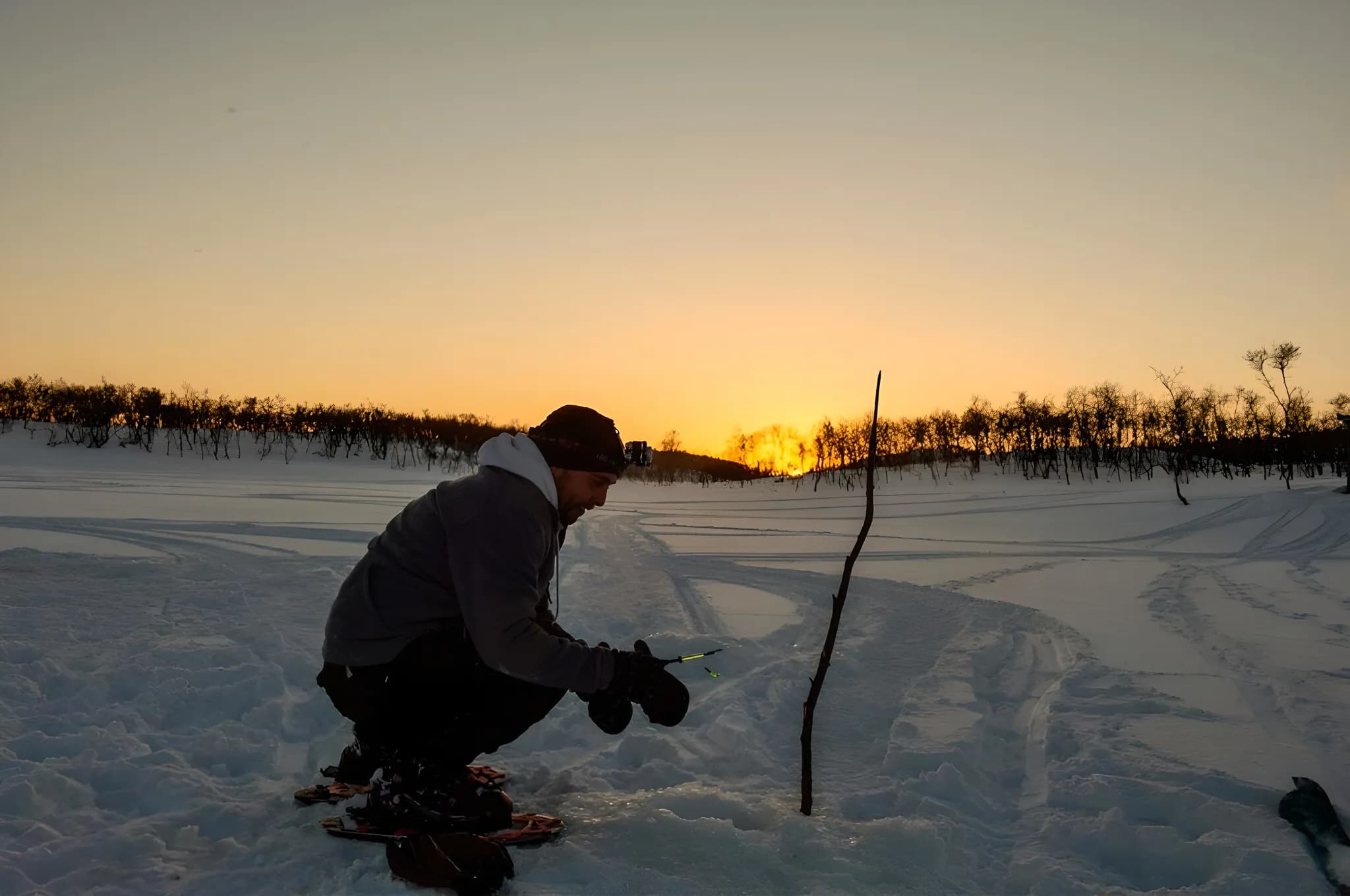 A man crouches in the snow at sunset, preparing for his expedition to Lapland.