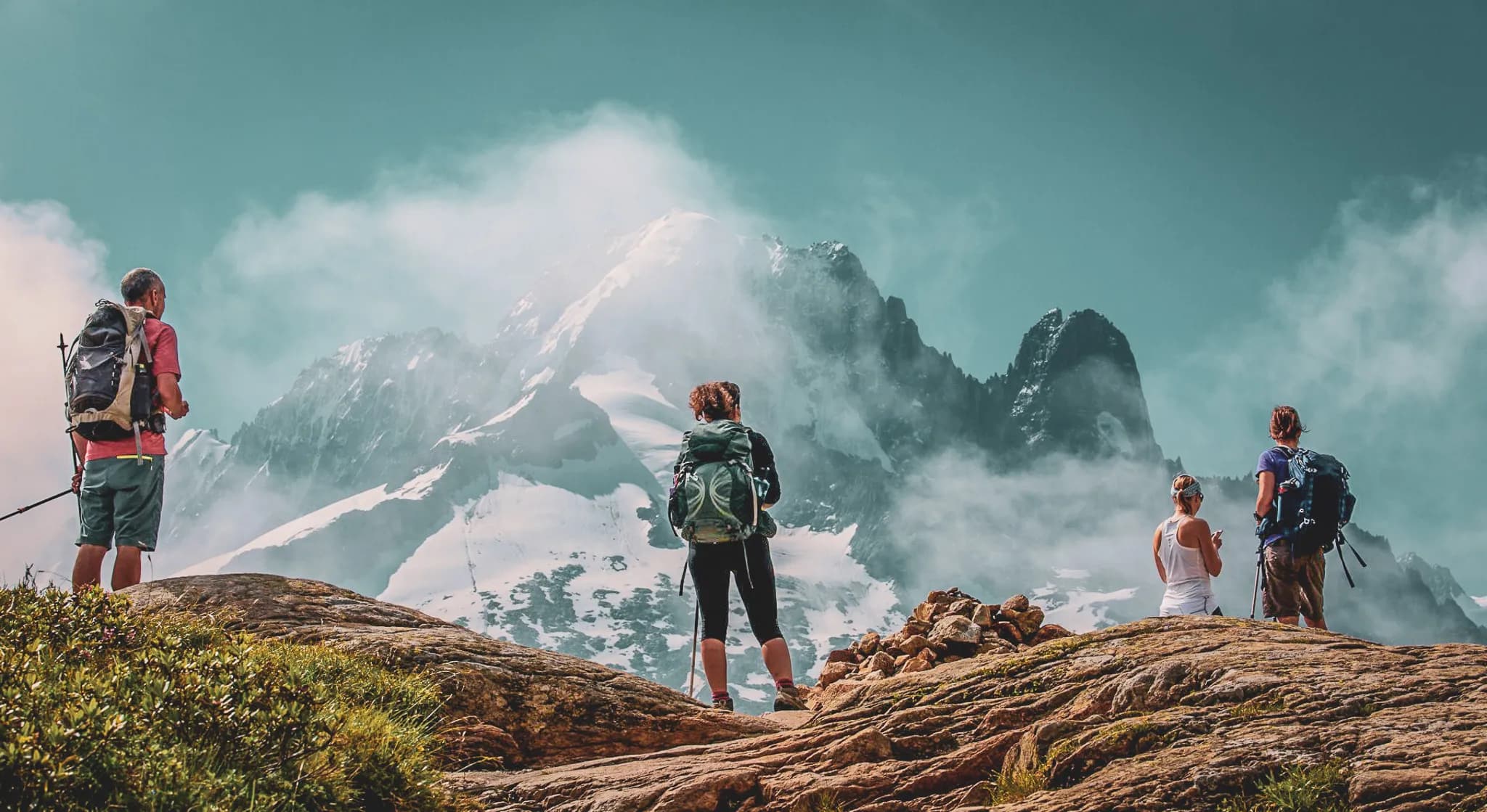 Un groupe de randonneurs se tient sur des rochers surplombant une majestueuse chaîne de montagnes. Certaines de ces montagnes sont enneigées, tandis que d'autres sont tapissées de rochers. Les randonneurs