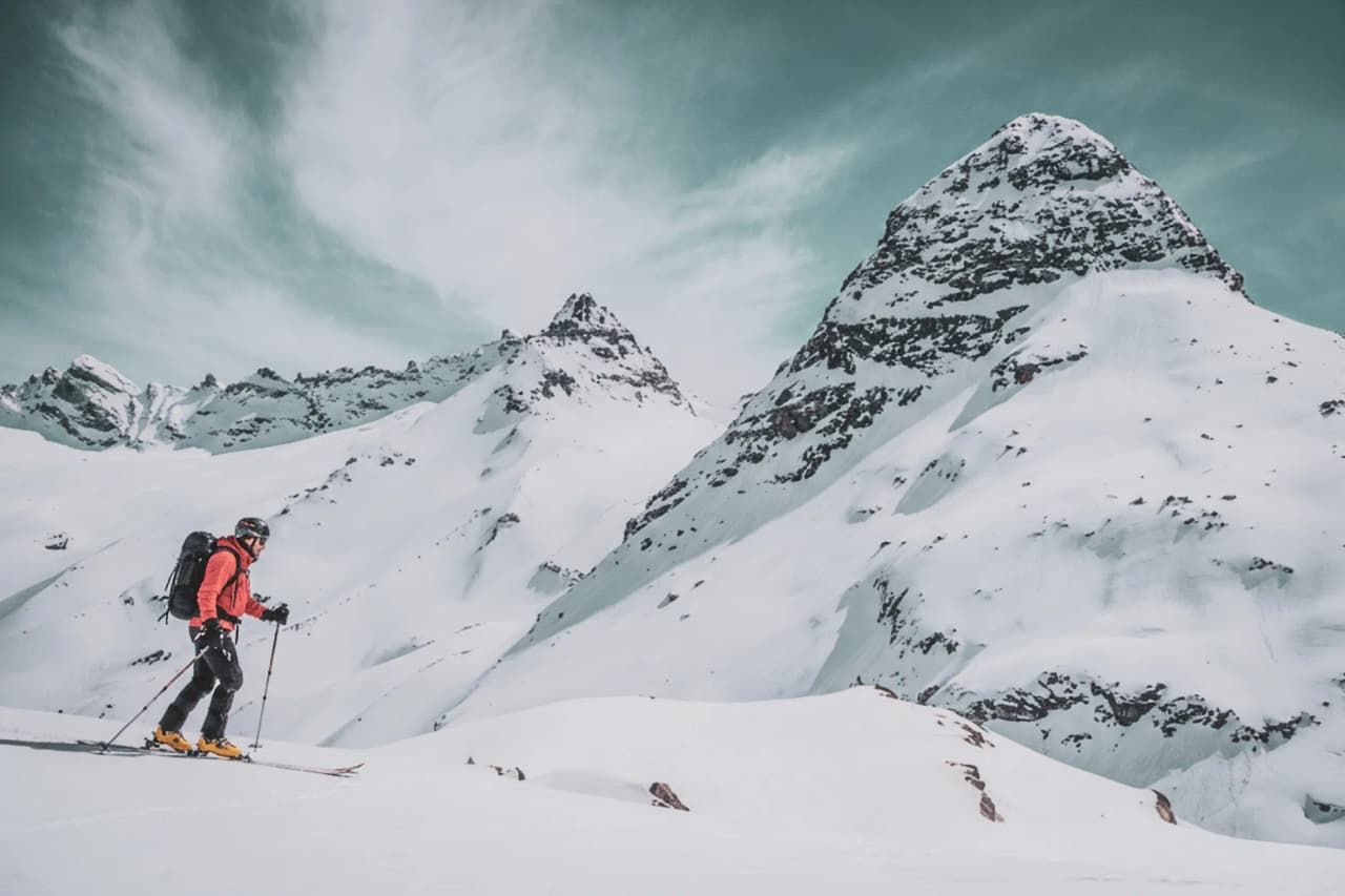 Skier in full ascent on snow-covered glaciers, majestic peak in background.