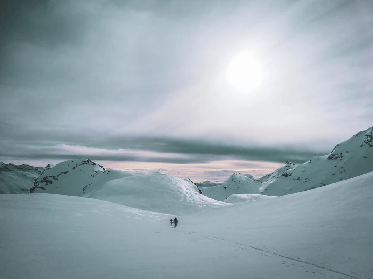 Two skiers light up in the heart of a majestic glacial landscape, under a cloudy sky.